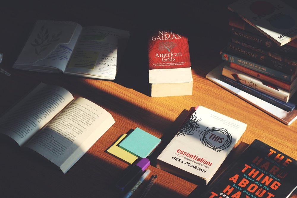 Open books, sticky notes and a pile of paperbacks on a wooden desk